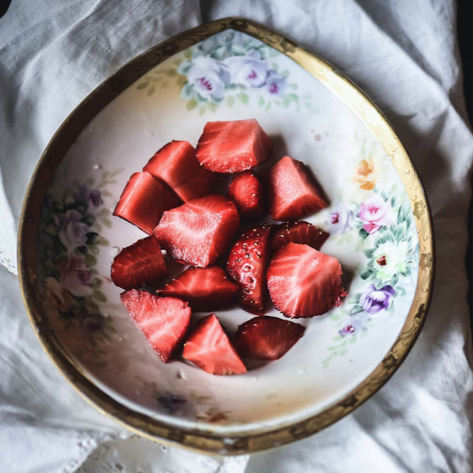Cut ripe strawberries in decorative floral bowl.