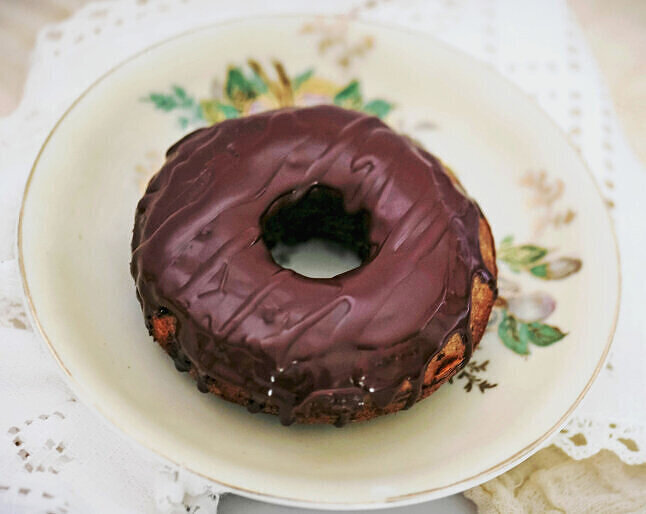 Homemade gluten free tigernut doughnut with chocolate glaze on floral plate.