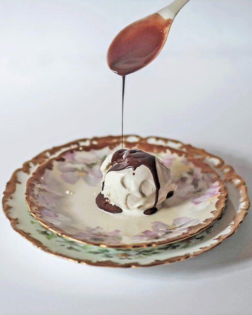 Spoon dripping chocolate sauce onto one scoop vanilla ice cream.