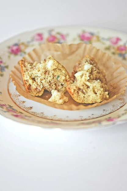 Pieces of feta thyme muffin in muffin wrapper atop decorative floral plate.