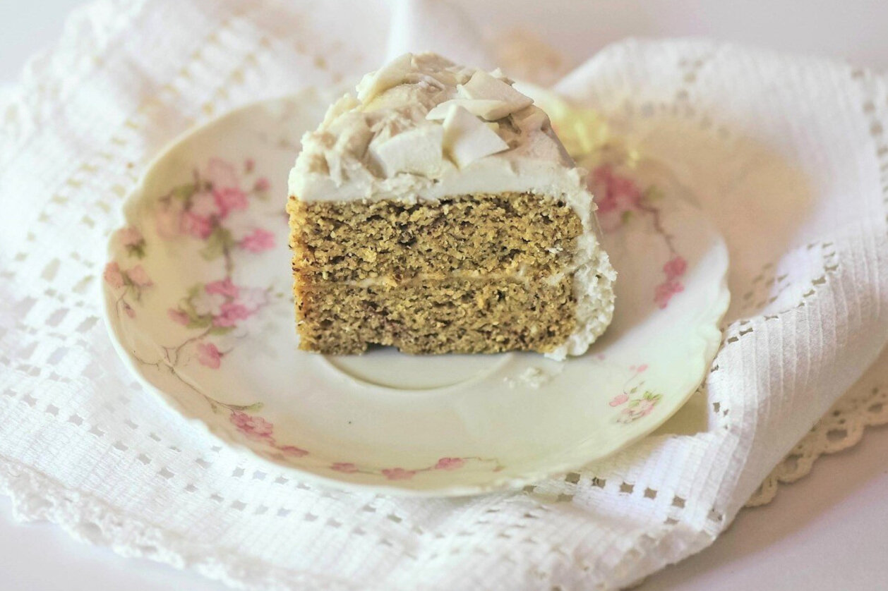 Slice of mini gluten free coconut cake with coconut flakes atop floral decorative saucer.