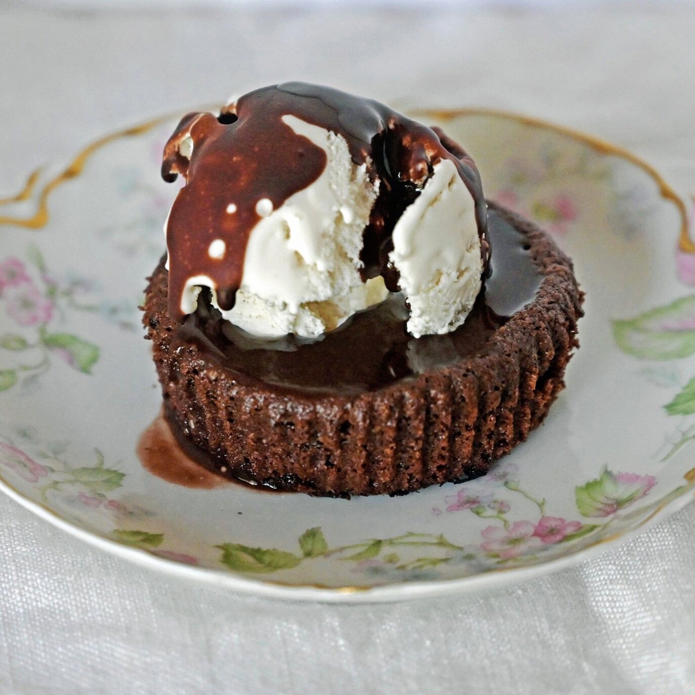 Gluten free brownie a la mode with homemade brownie base and a scoop of vanilla ice cream covered in chocolate sauce.