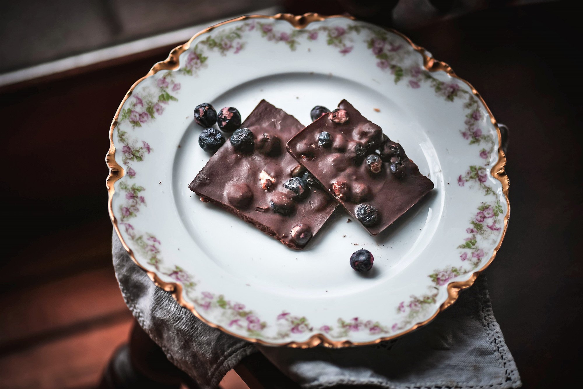 Homemade chocolate bark with matcha and freeze dried blueberries on decorative floral plate.