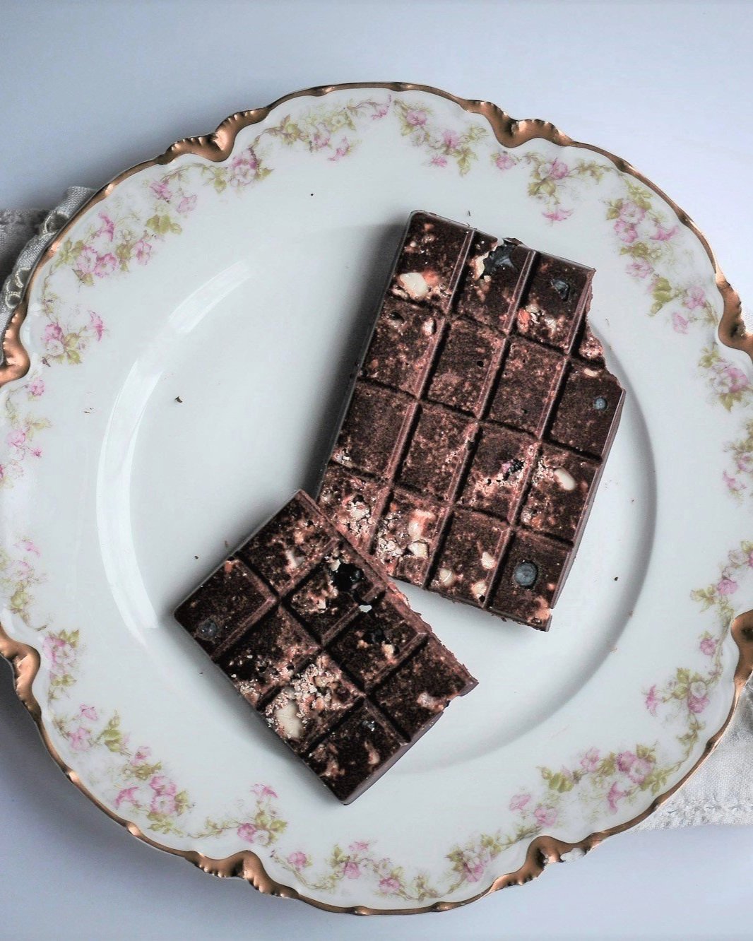 Homemade chopped almond chocolate bar broken in half atop decorative plate.