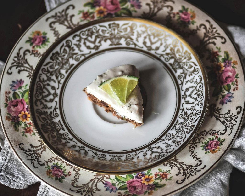 Slice of vegan lime pie with lime piece on top atop two decorative stacked plates.